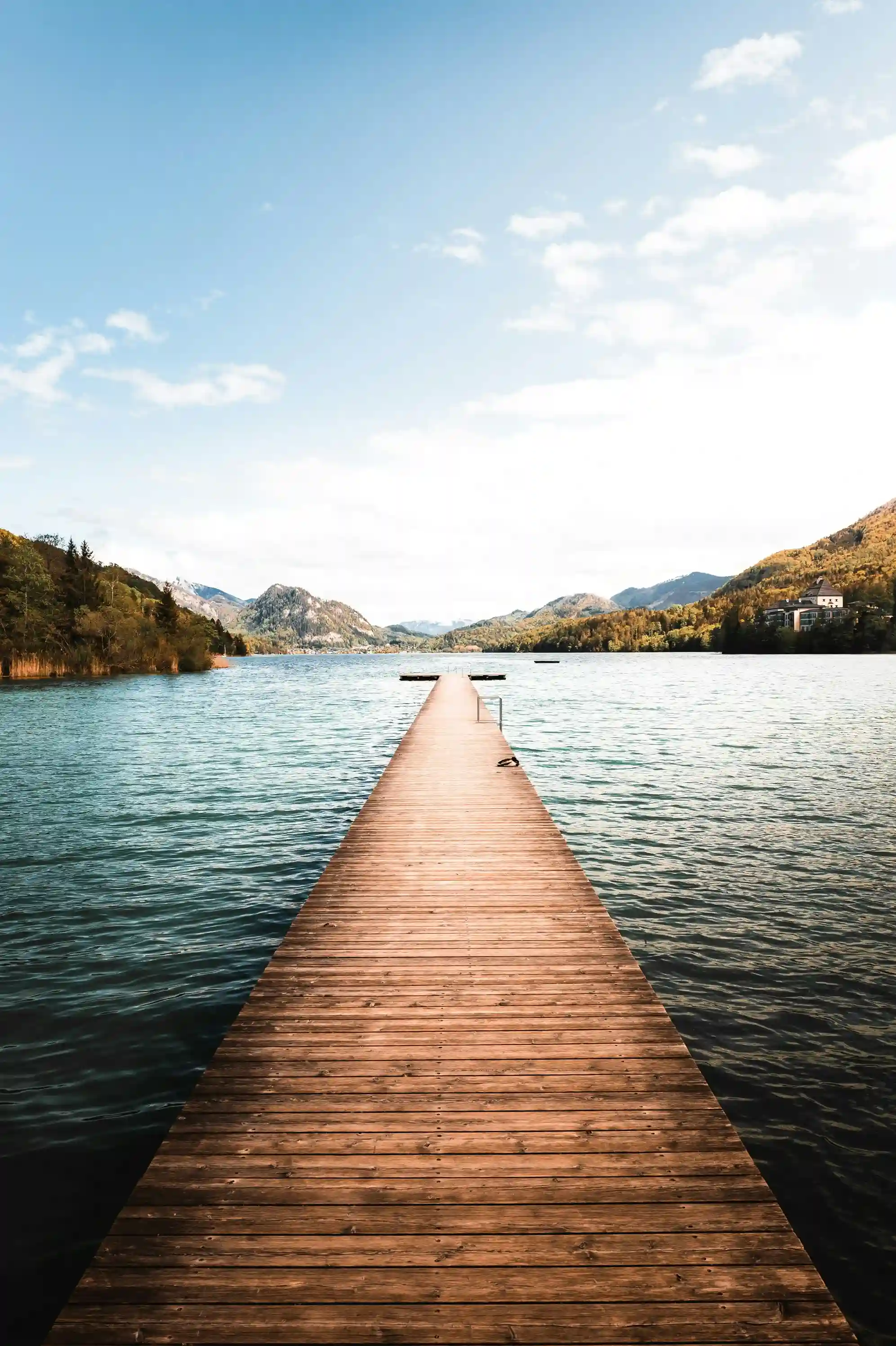 Wooden dock stretching into a calm lake surrounded by forested hills under a blue sky.