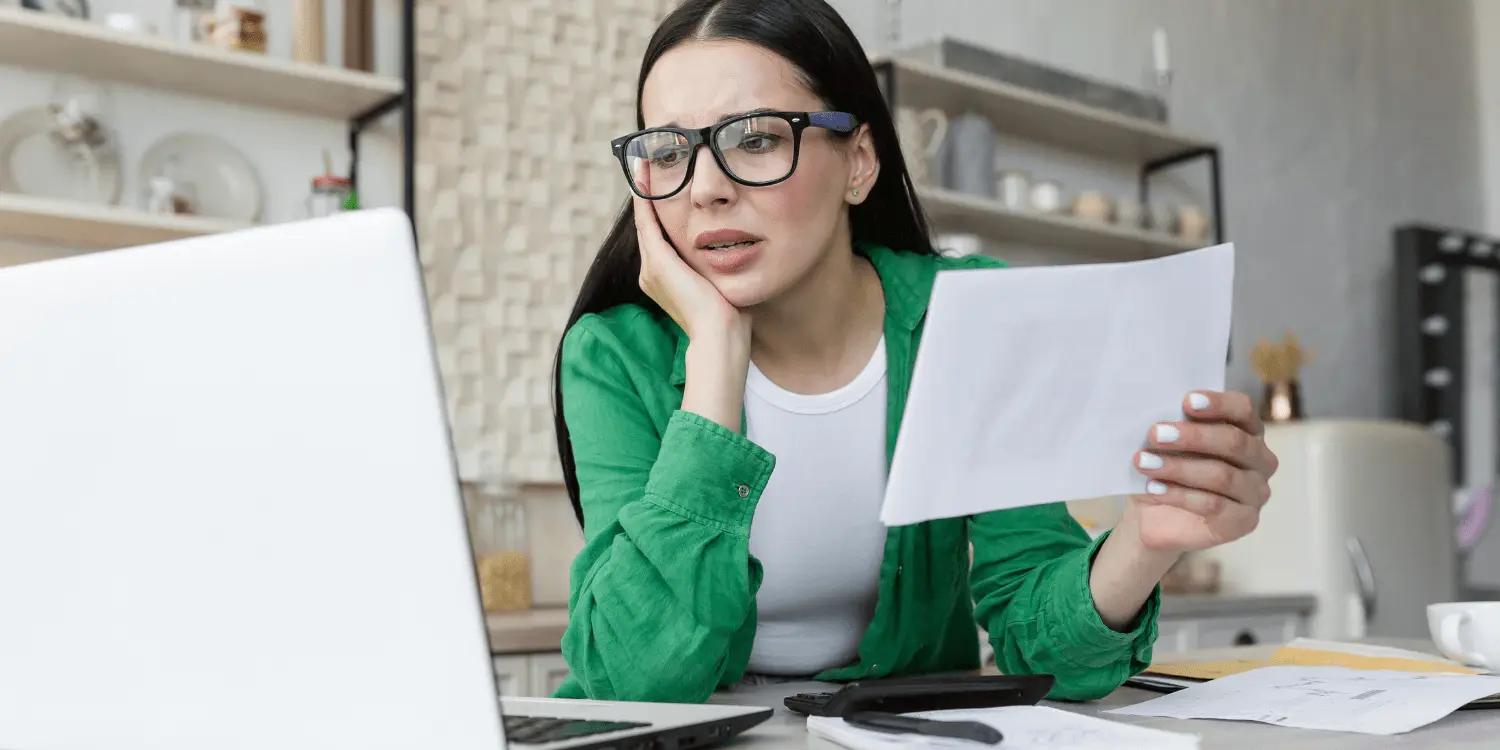 Woman with glasses sitting at desk, holding paper distressed over a bad loan.