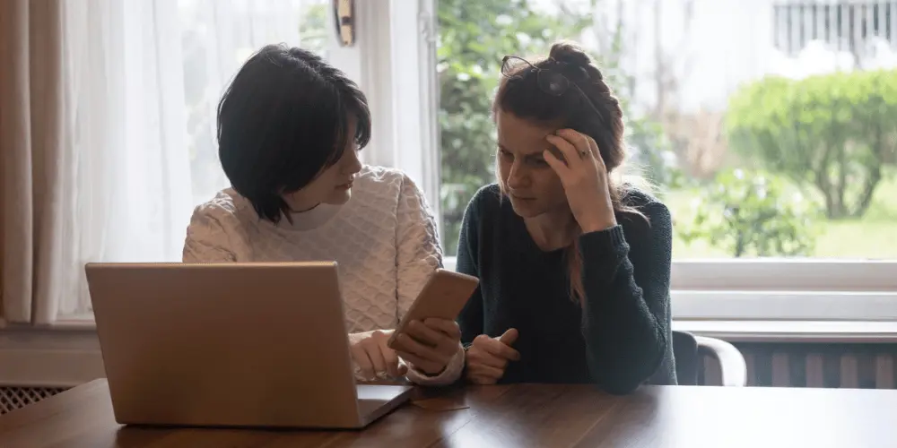 A friend demonstrating compassion to a friend at the kitchen table with a laptop in front of the laptop due to a password protection vulnerability.