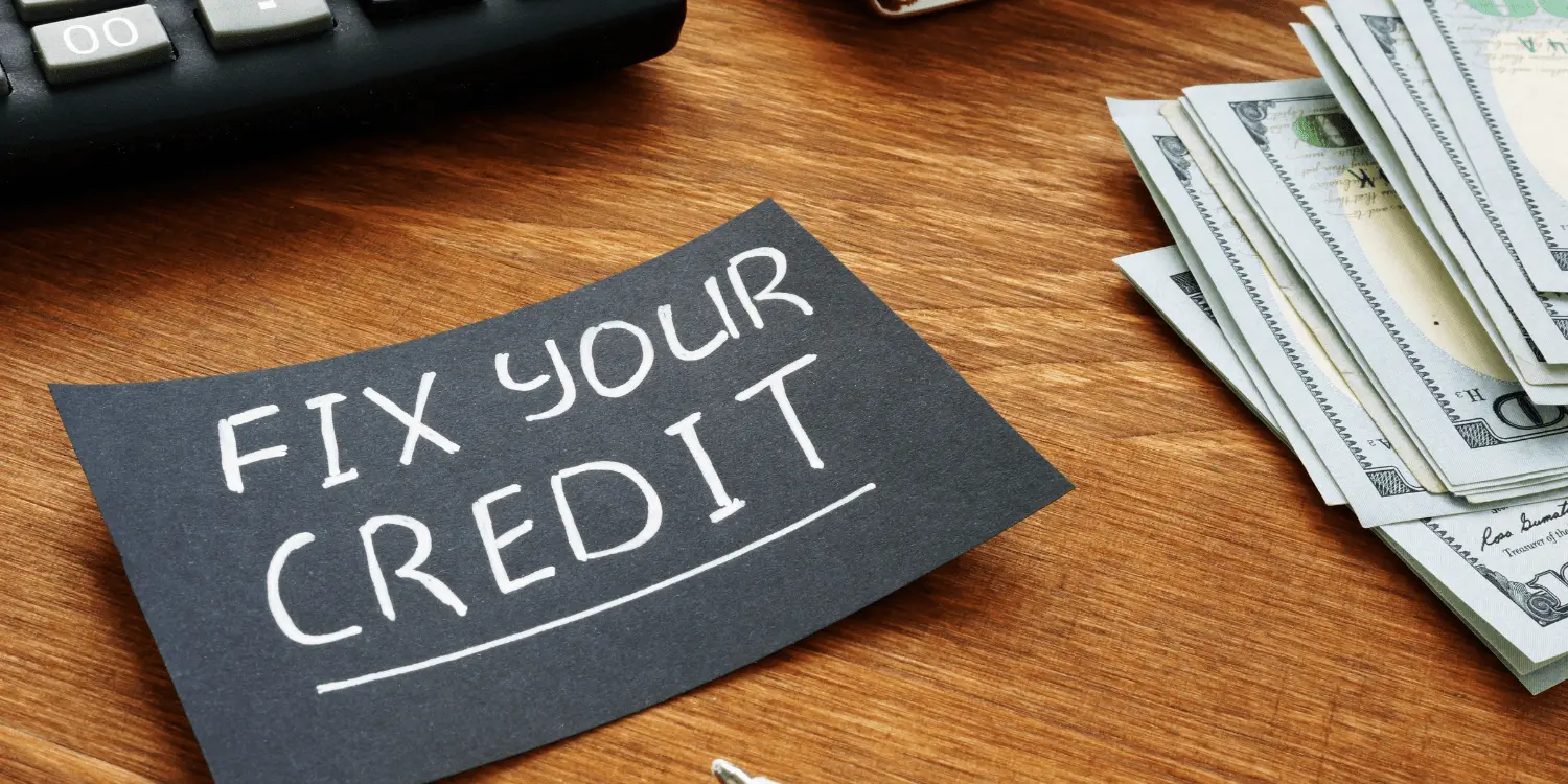 A black paper with white fix your credit written on it as it lays on top of a desk.