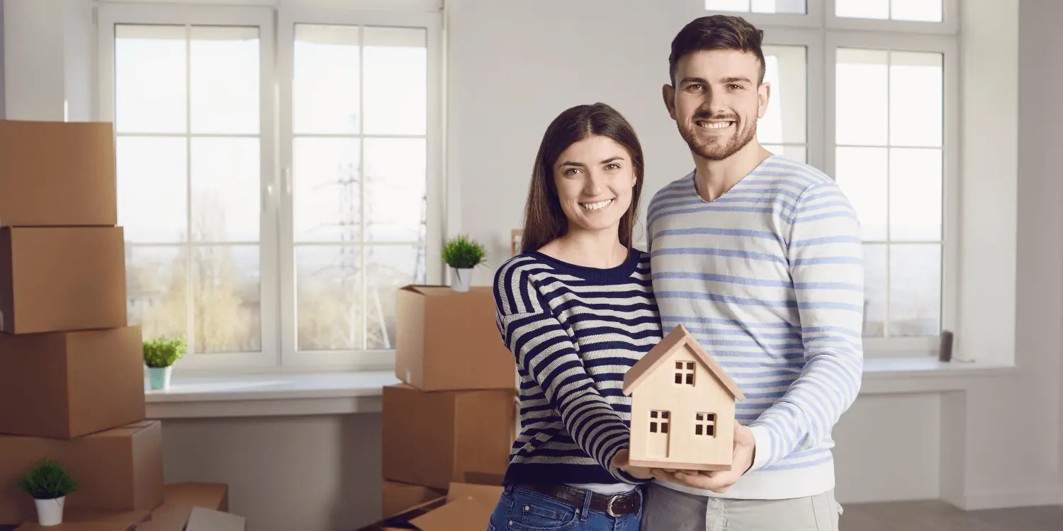 A couple holding a model house in the house the moved into while renting an apartment.