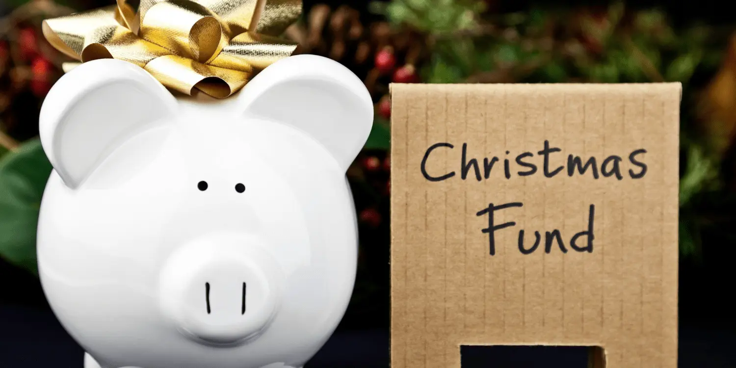 A donation box with "Christmas Fund" written on it, surrounded by holiday decorations and piggy bank with a bow on it.