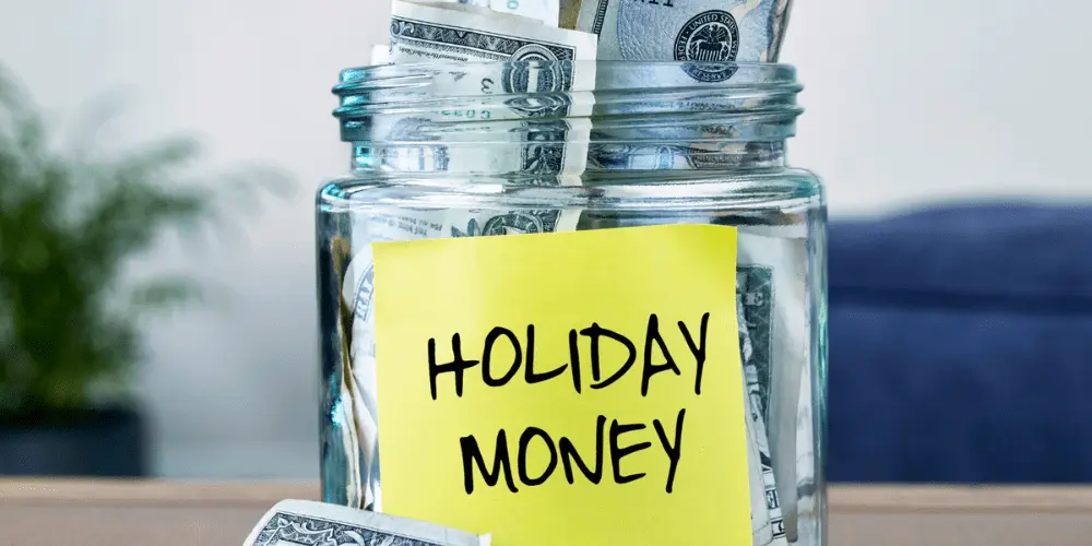 A jar that is labeled "holiday money" and having money within the glass jar.