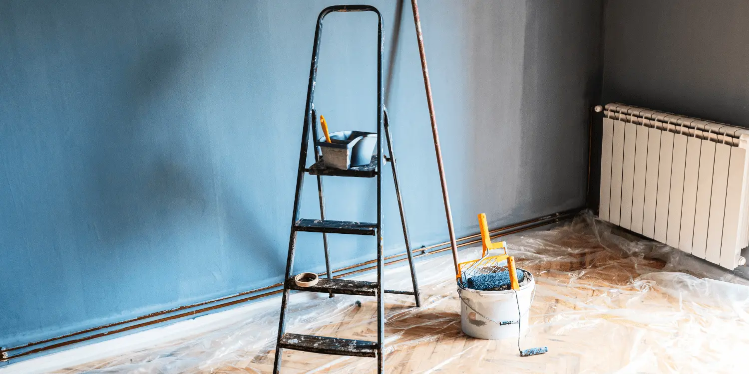 A ladder and paint bucket on a wooden floor, ready for a renovation project to help increase the value of a house.
