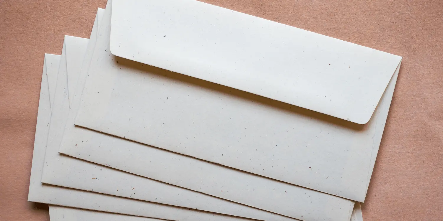 A pile of white envelopes against pink backdrop ready for hardship letters to be inserted into them. 