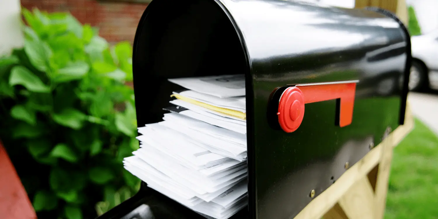 A stack of junk mail and bills inside a black mailbox outside of a house. 