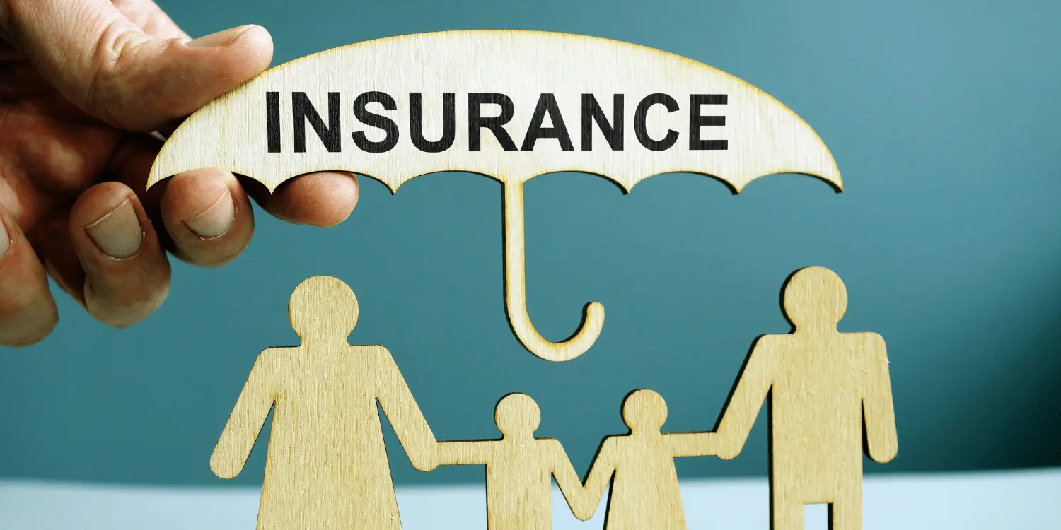 A hand holding up a cardboard umbrella with the word insurance on it covering a family carved out of cardboard to illustrate insurance protection.