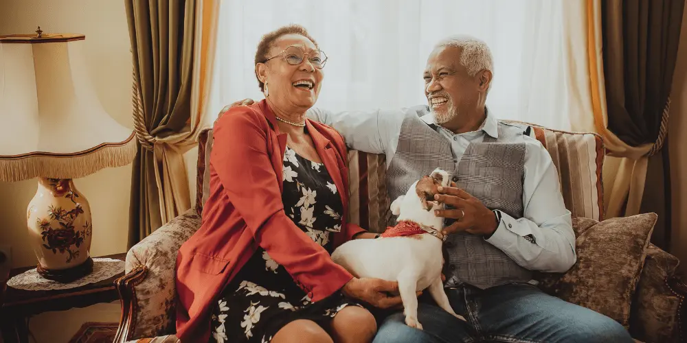 An older couple and their dog sit on a couch, engaged in conversation about the benefits of a reverse mortgage.