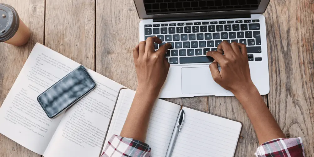 An individual that is researching online about reverse mortgage options on a computer with a note book to the left of the individual.