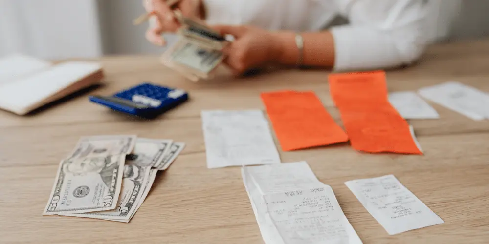 A person counting money on their table with calculators, pencils, and paper covering the table as they manage their income and bill payments.
