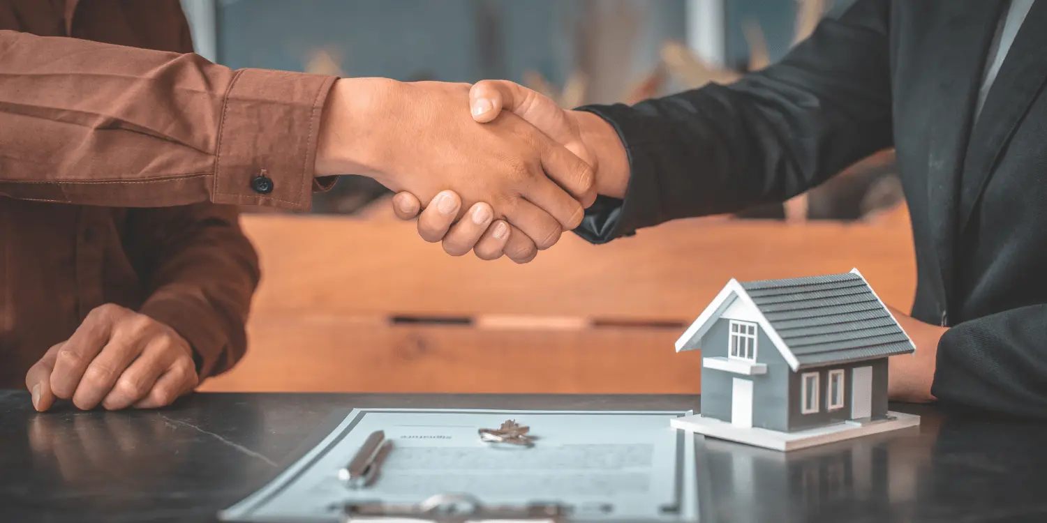 Two people shaking hands over a house model, symbolizing an agreement on a type of home loan.