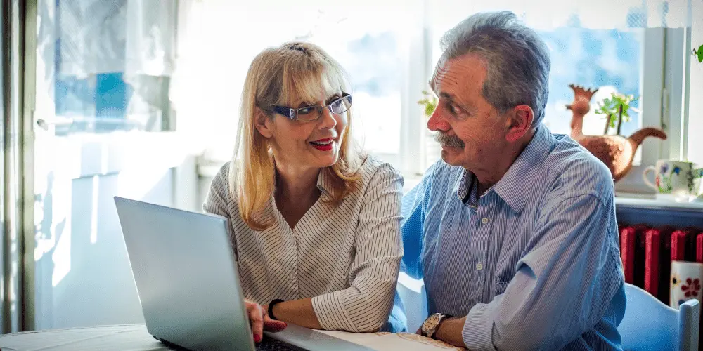 Senior couple researching HECM reverse mortgages on a laptop, learning what they are and how they work for financial security.