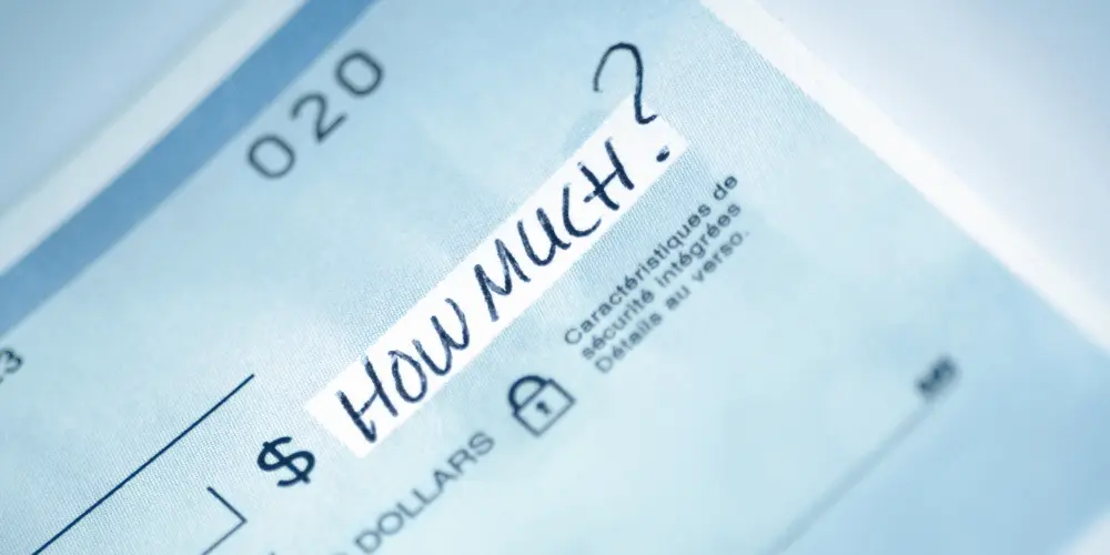 Primer plano de un cheque con la pregunta «¿Cuánto?» escrito, simbolizando el alquiler asequible y las decisiones presupuestarias inteligentes para la vivienda.