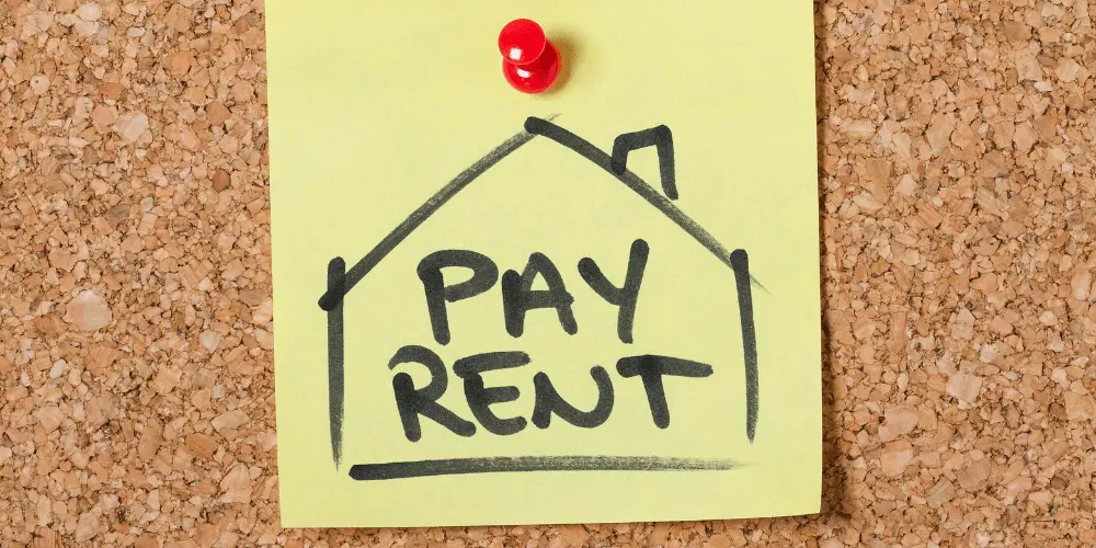 Pay Rent message on sticky note, symbolizing financial strain and rental help for paycheck-to-paycheck families.
