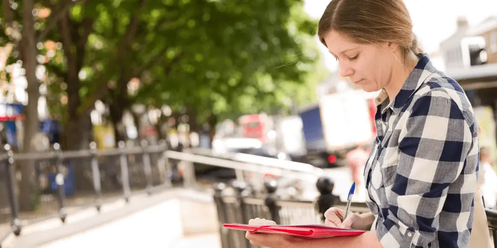 Persona que escribe en un portapapeles al aire libre y prepara documentos para una solicitud de asistencia por desastre de la FEMA después de un desastre.
