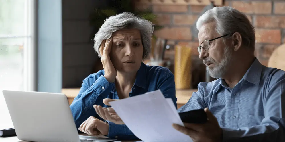 Concerned senior couple reviews reverse mortgage papers on laptop, exploring recovery options after a possible loan default.