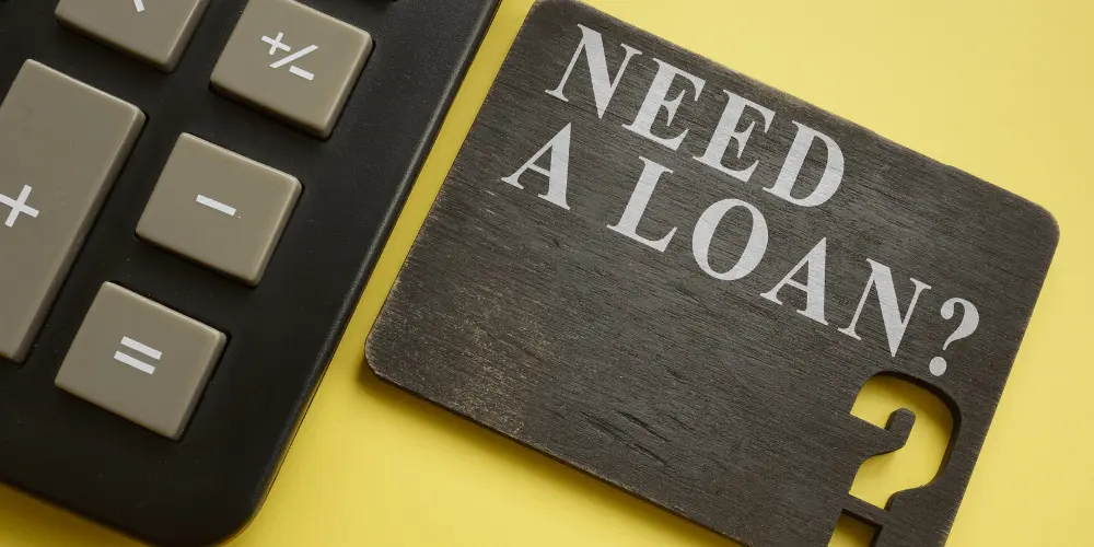 Calculator beside a “Need a Loan?” sign representing SBA disaster loan eligibility and credit score impact.