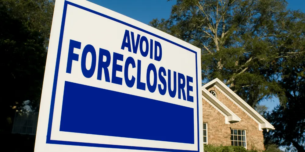 Blue and white avoid foreclosure sign outside a house symbolizing mortgage help and home protection.