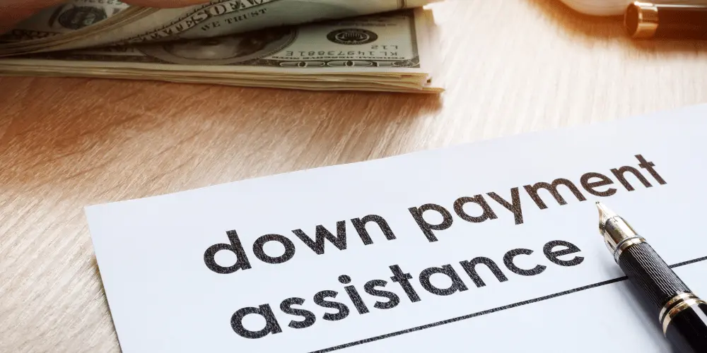 Document labeled down payment assistance next to cash and pen representing homebuyer aid programs.
