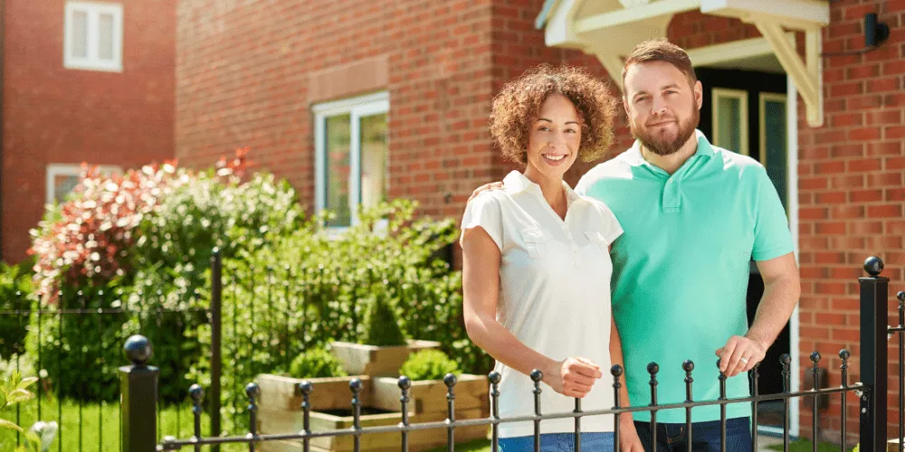 A happy couple standing outside their new home, showing what Fannie Mae’s updated rules can mean for first-time buyers.