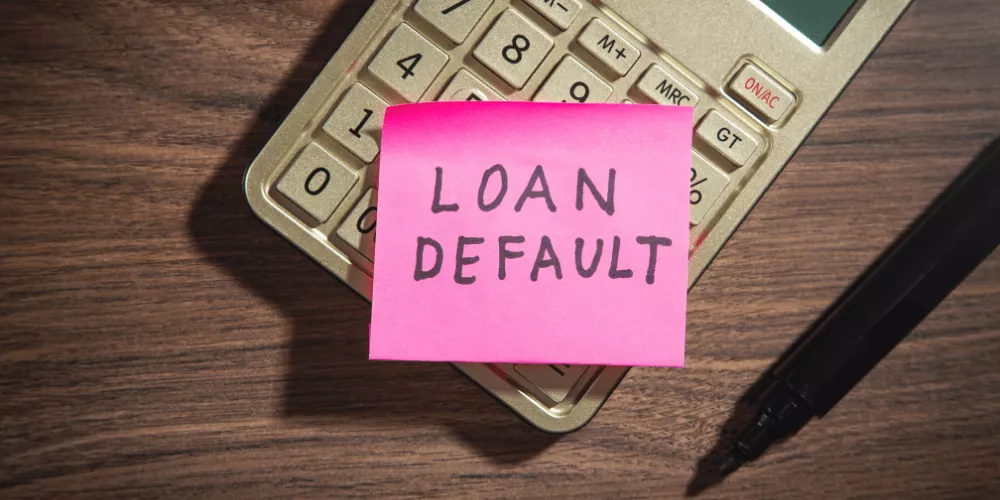 Nota rosa en la que se lee «Incumplimiento del préstamo» en una calculadora, destacando el grave impacto financiero de la falta de pago de los préstamos estudiantiles.