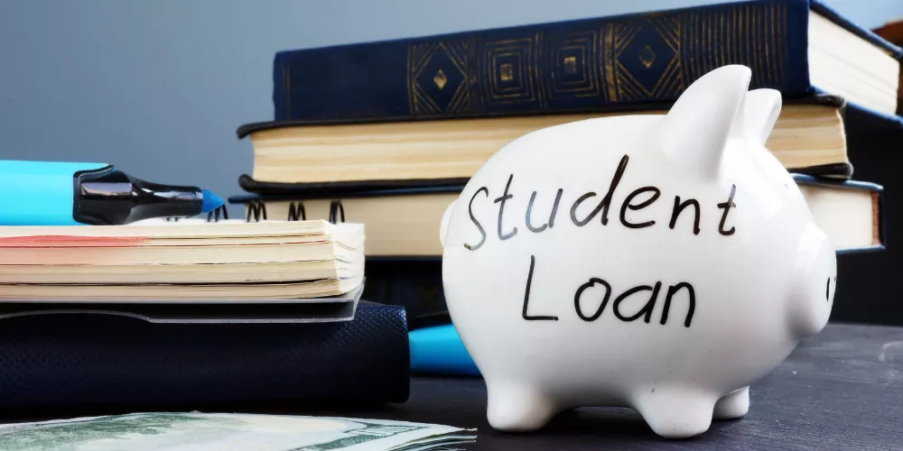 Piggy bank labeled ‘Student Loan’ beside books and papers, showing how missed payments can lead to student loan default.