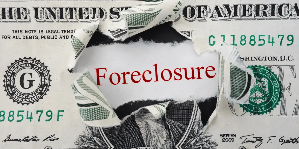 Torn dollar bill revealing the word ‘foreclosure,’ symbolizing the financial impact of falling behind on mortgage payments.