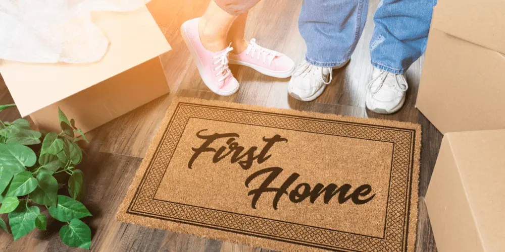 A welcome mat reading “First Home” as new buyers move in, symbolizing house hacking as a way to make a first mortgage more affordable.