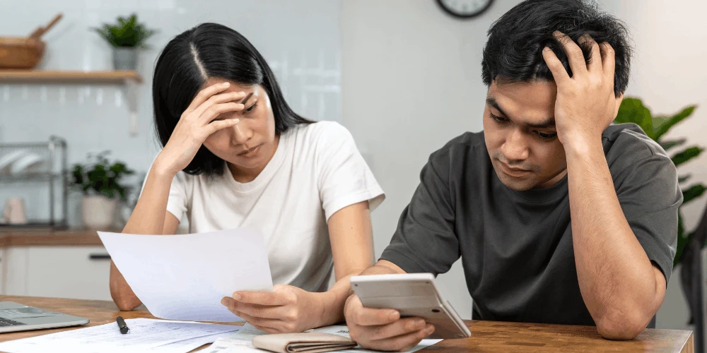 Couple reviewing bills and a calculator, showing how charged-off debt affects finances and what steps may come next.