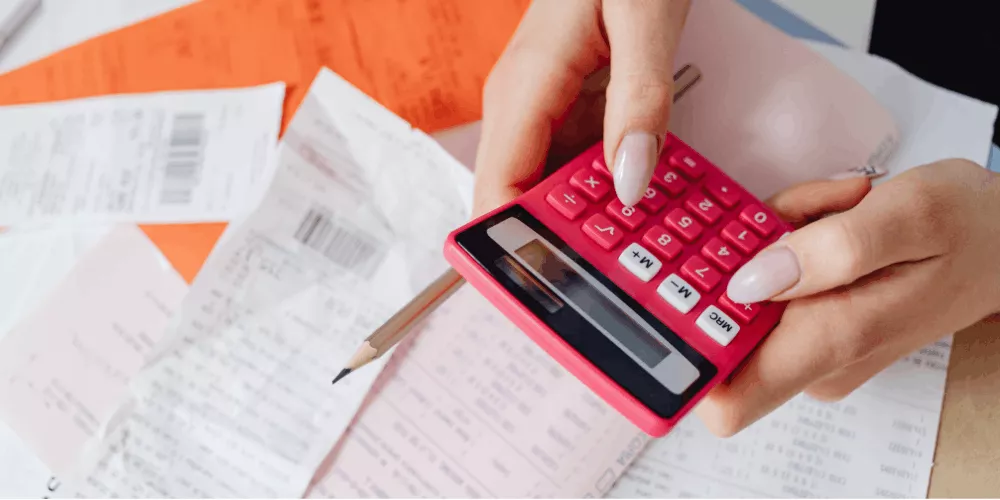 Person calculating bills and receipts on a calculator while reviewing expenses and figuring out how to manage debt payments.