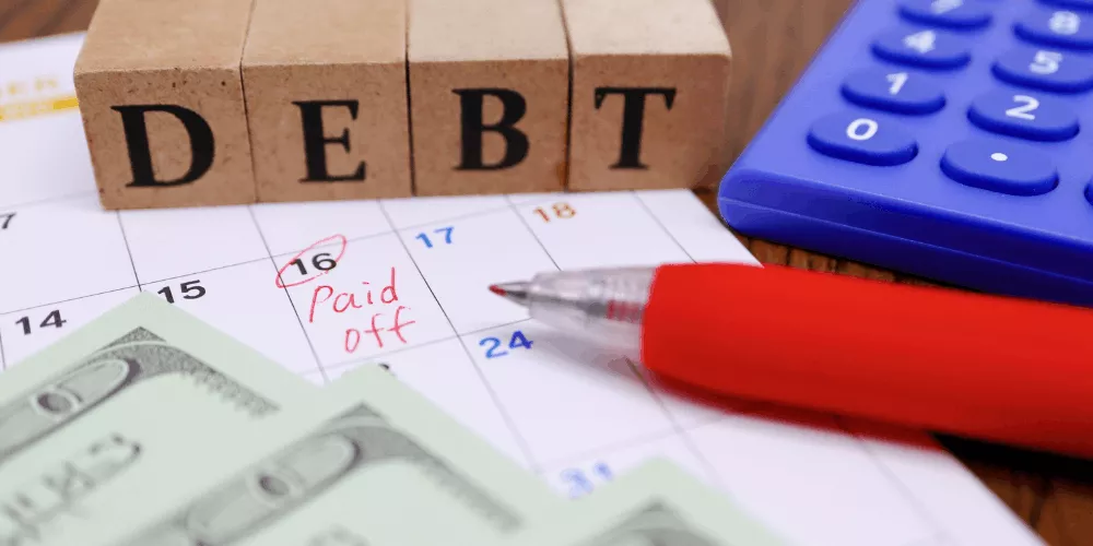 Calendar marked “paid off” with cash, calculator, and debt blocks showing the process of planning debt payments and reducing balances.