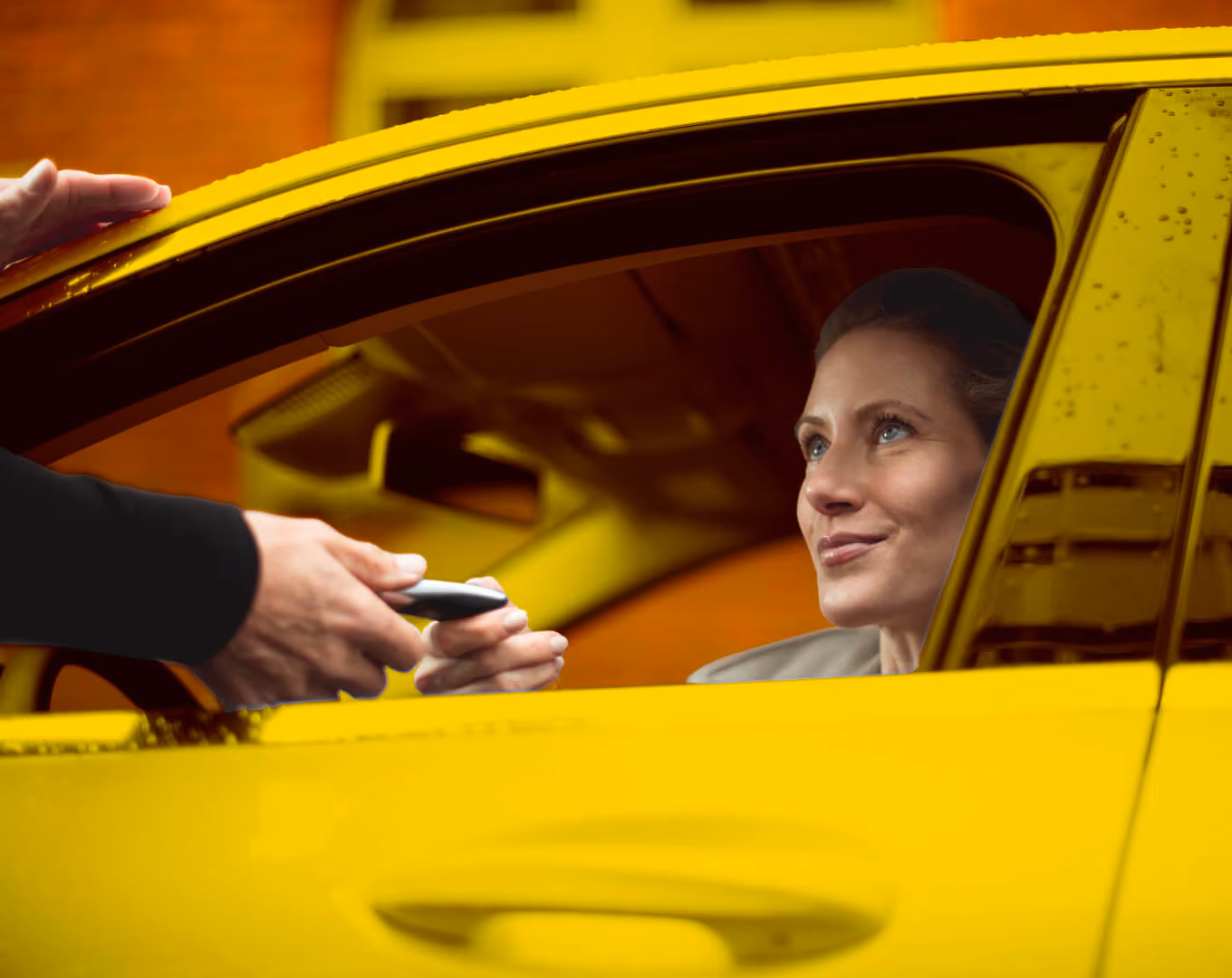 Frau im gelben Auto nimmt lächelnd einen Autoschlüssel durch das Fenster entgegen