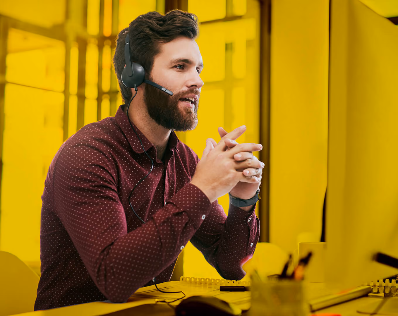 Mitarbeiter mit Headset sitzt am Schreibtisch und spricht mit einem Kunden am Telefon