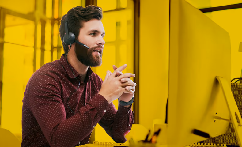 Ein freundlicher Mann sitzt mit einem Headset am Computer und telefoniert gerade.