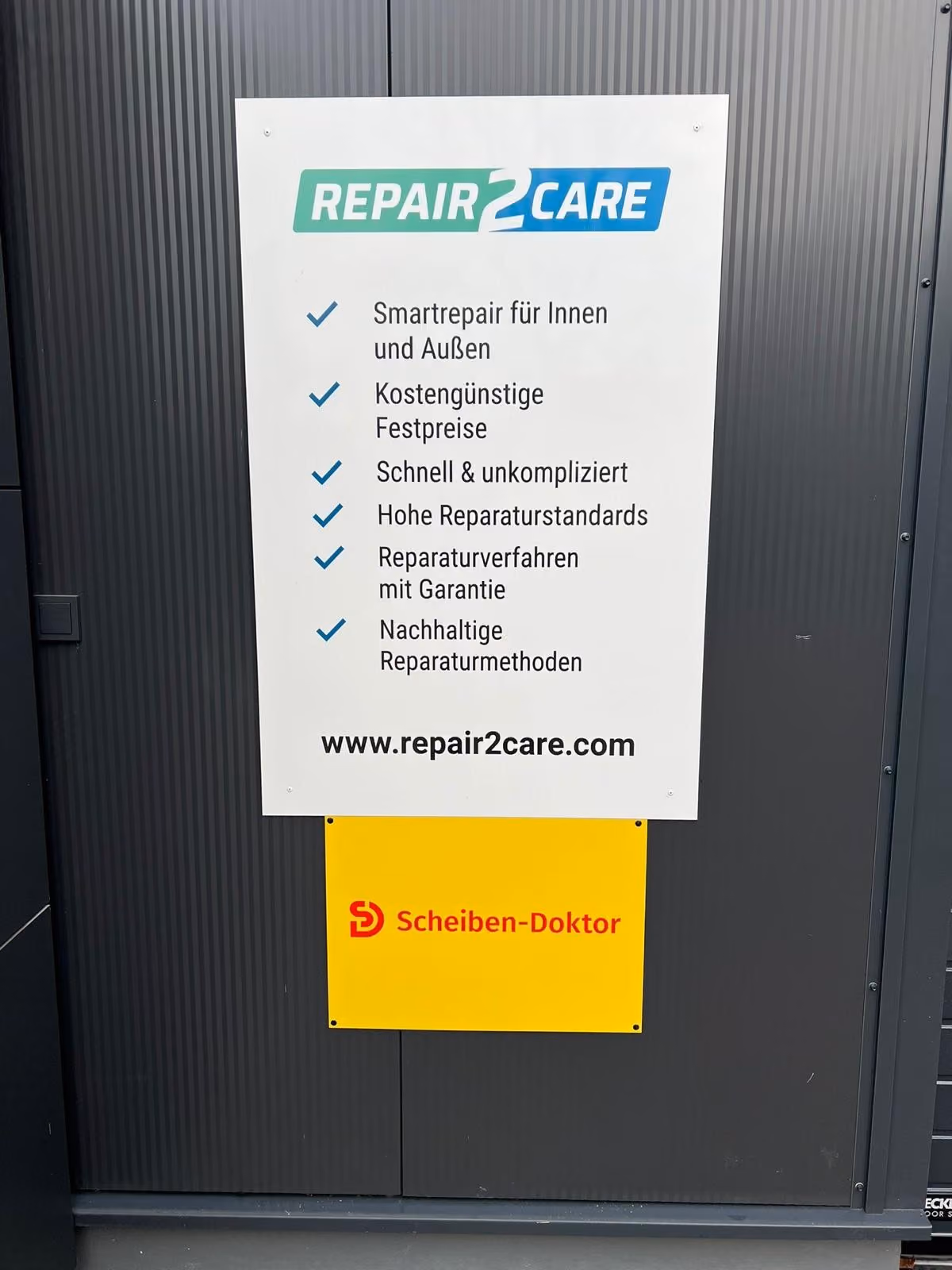 Repair2Care-Schild mit Leistungen über einem Scheiben-Doktor-Schild an der Fassade
