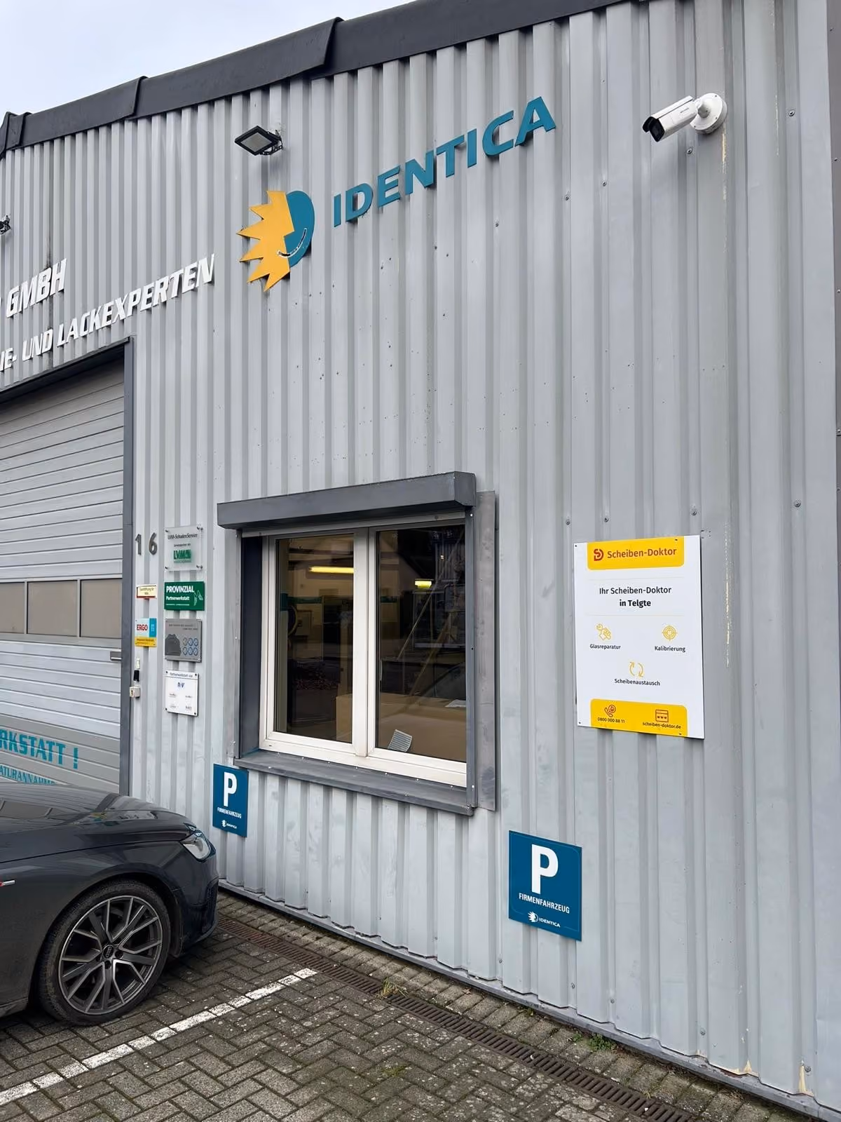 Werkstattfassade mit Identica-Logo, Parkplatzschildern und Scheiben-Doktor-Schild für Telgte