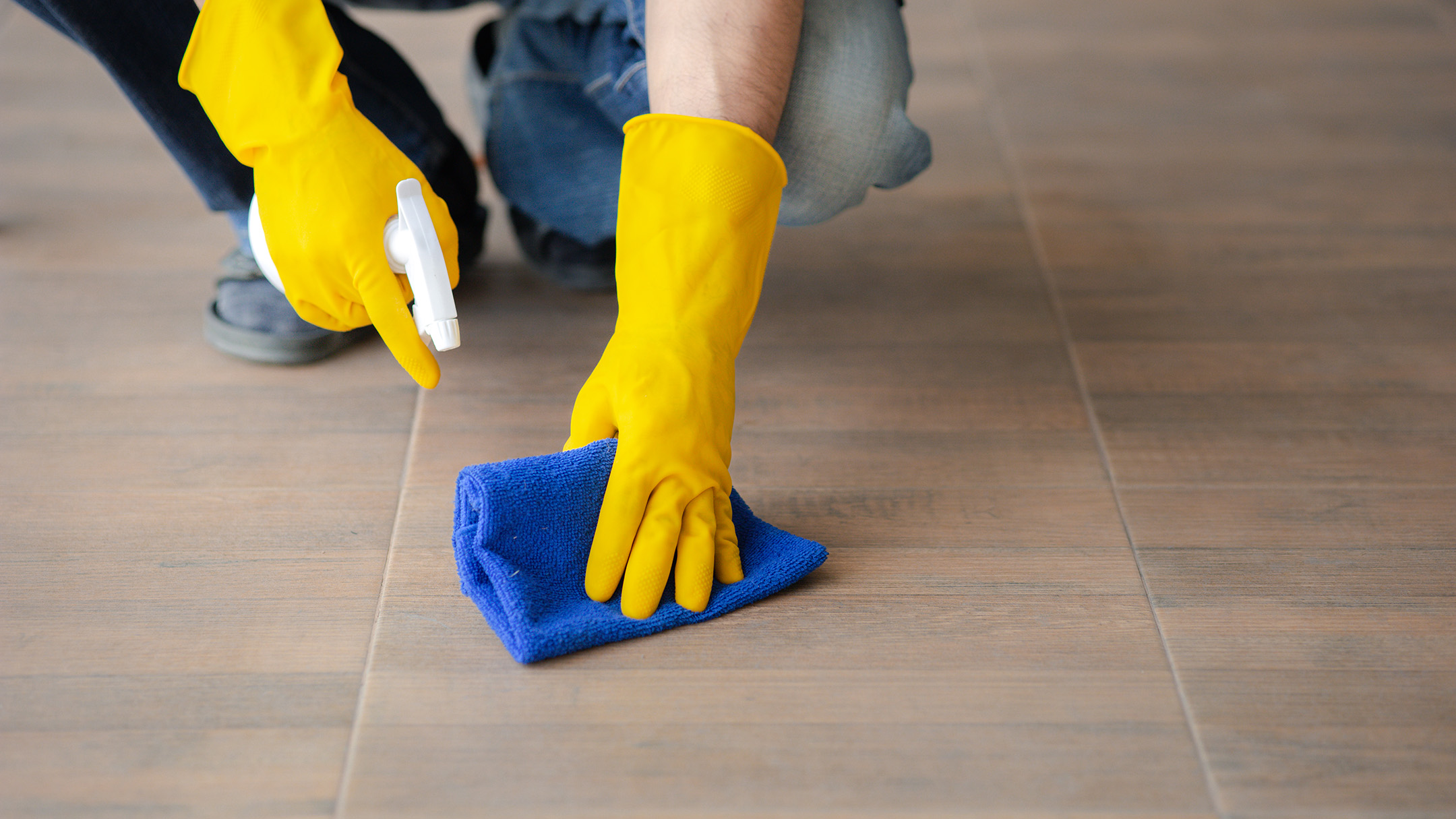 A hand with yellow gloves, cleaning the floor.