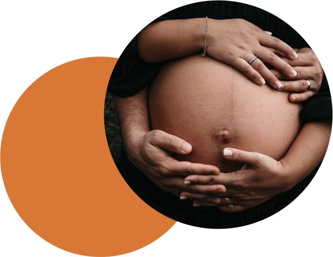 A lady resting her hand on top of her pregnant belly whilst a person holds her from behind