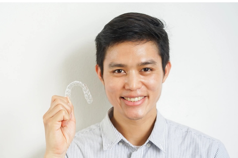 Smiling man holding a clear dental aligner against a white background.