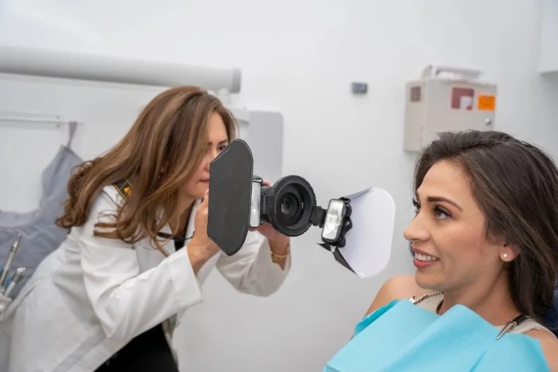 Dr. Streett in a white coat takes a close-up photograph of a smiling female patient wearing a dental bib.