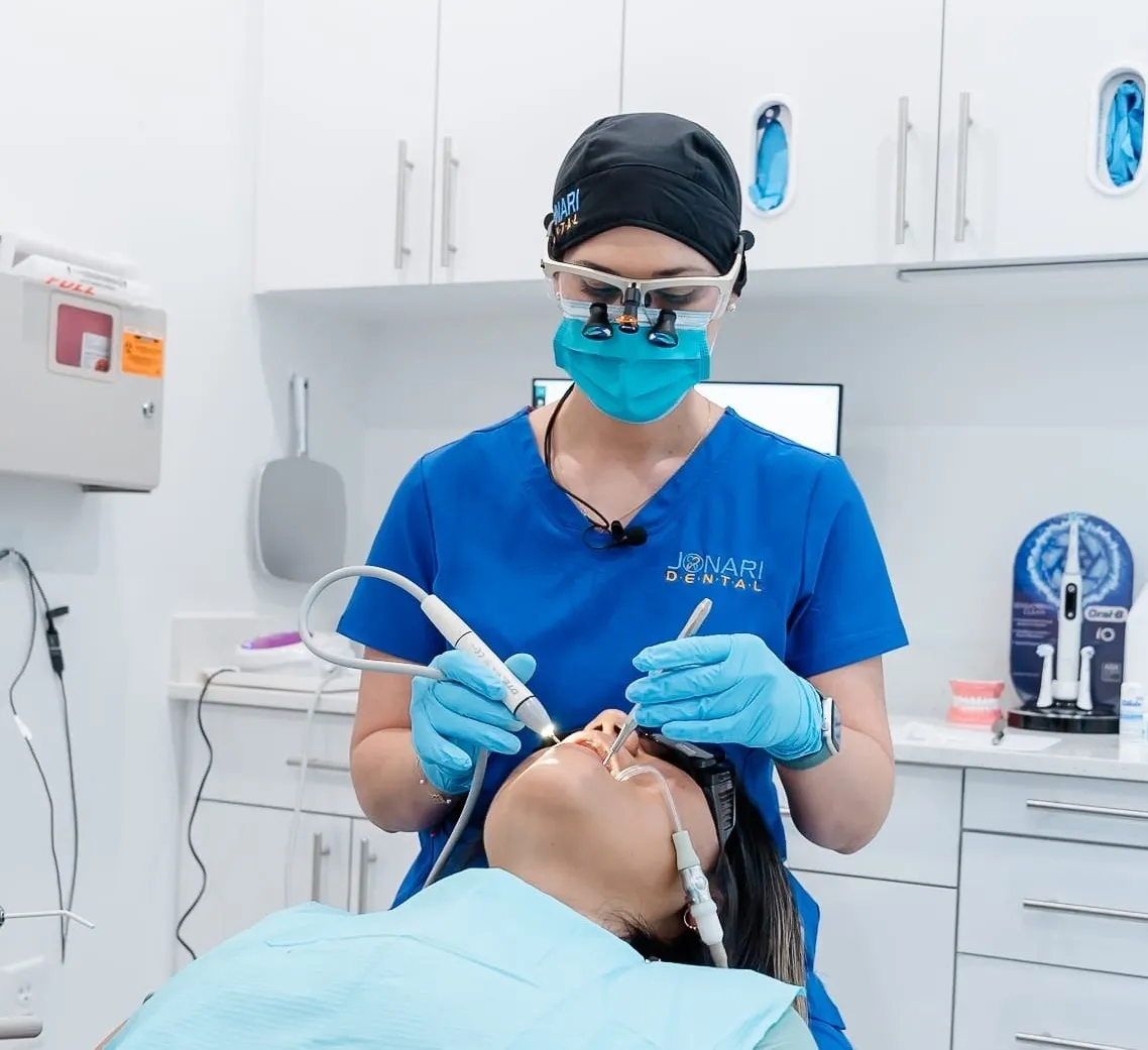 Dental professional in blue scrubs and protective gear performing a periodontal treatment on a patient reclining in a dental chair at Jonari Dental of Cooper City.