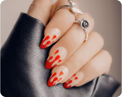 Hand with almond-shaped nails featuring beige polish and red flame nail art, wearing a silver ring, resting on black leather.