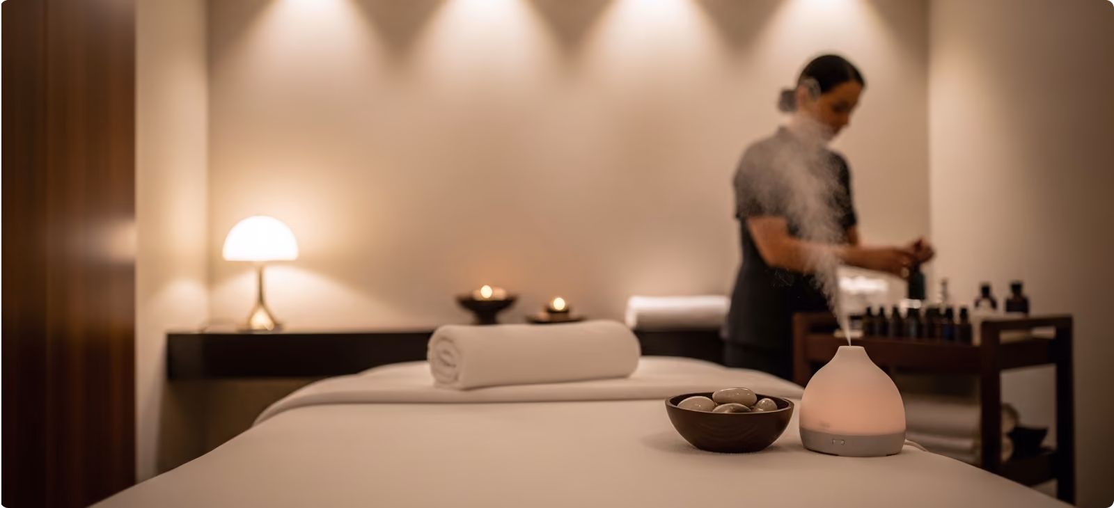 Massage table with neatly folded towels in a warmly lit spa or wellness room with plants and modern furniture.