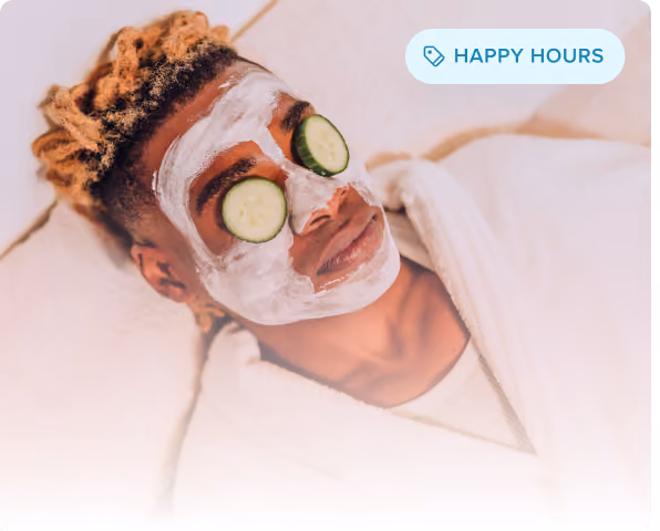 Hombre sonriente con los ojos cerrados y una máscara facial negra aplicada, relajándose sobre una superficie de color beige.