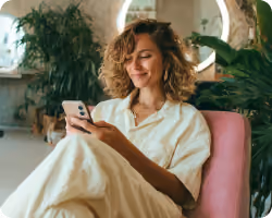 Surprised woman with curly hair talking on a yellow retro phone, wearing a colorful patterned shirt.