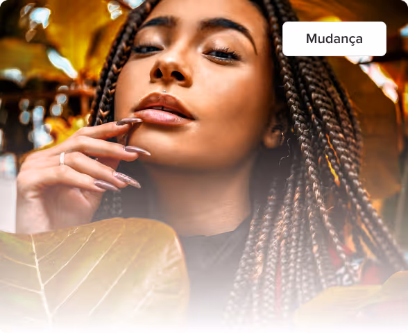 Close-up de uma mulher com cabelos trançados e unhas bem cuidadas posando cuidadosamente com folhas de outono em primeiro plano.