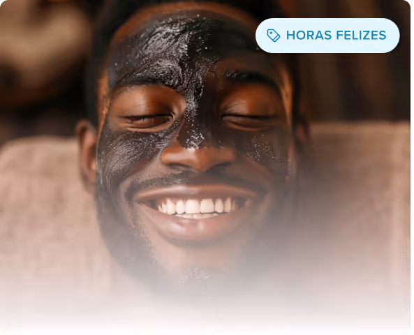 Homem sorridente com uma máscara facial preta deitado com os olhos fechados, desfrutando de um tratamento de spa.