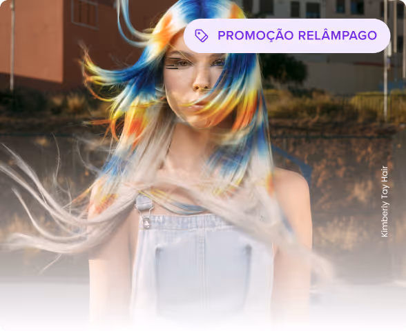 Mulher com cabelos longos e soltos tingidos nas cores vibrantes de azul, amarelo e laranja, vestindo um macacão jeans claro.