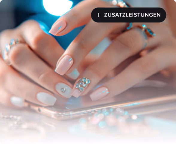 Close-up of hands with manicured nails featuring light pink polish and rhinestone decorations, resting on a smartphone.