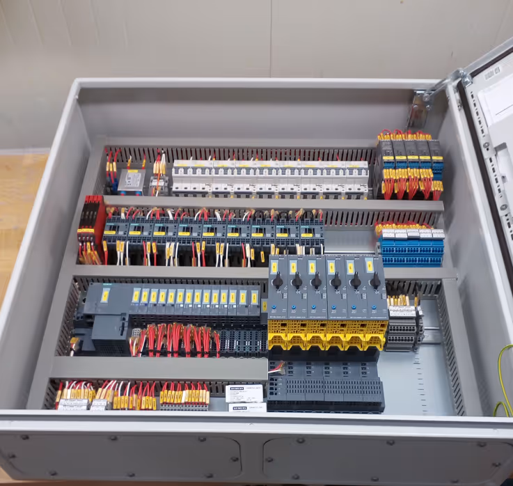 Open industrial electrical control panel with neatly organized wires, circuit breakers, and various terminal blocks.